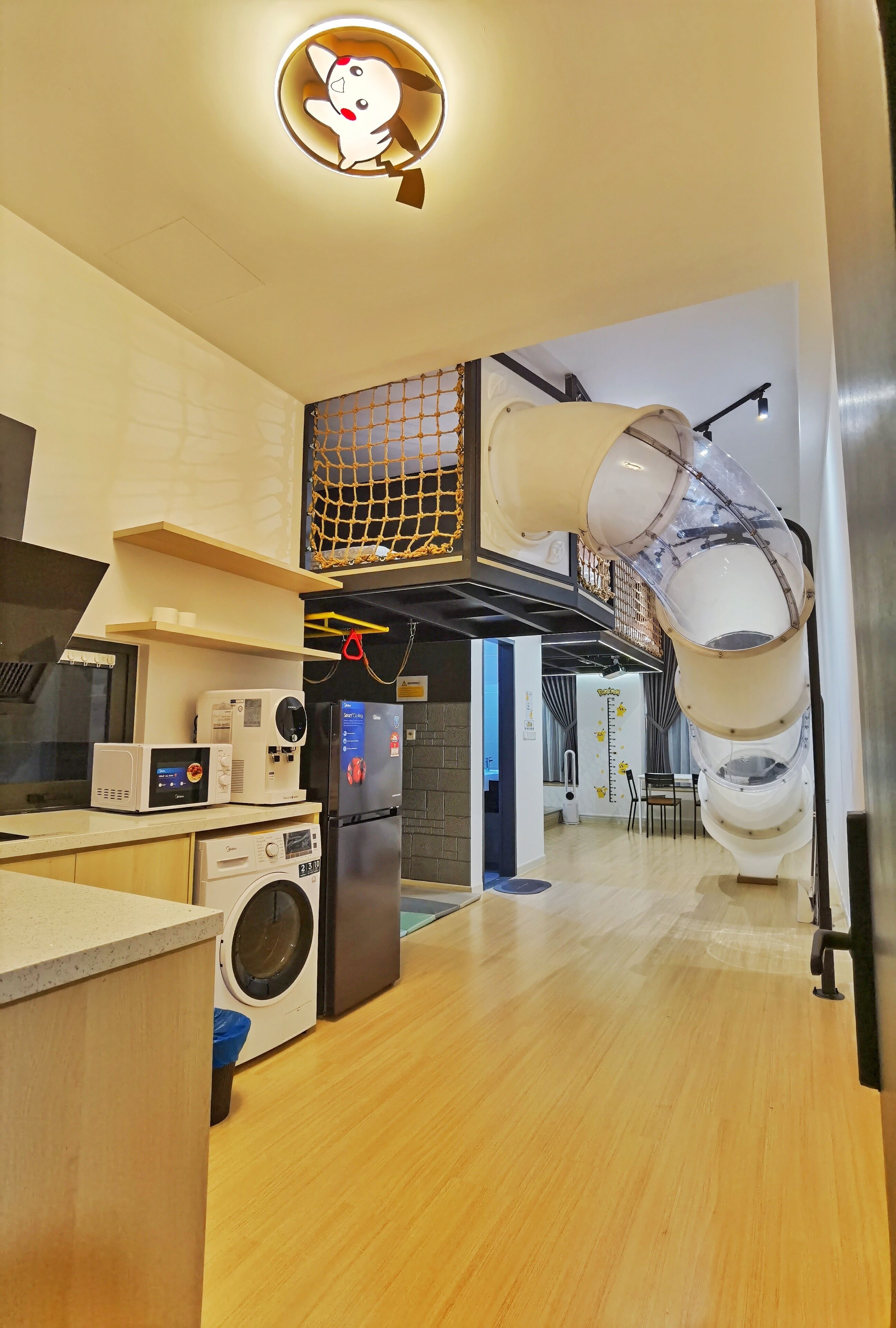 Een moderne keuken met een magnetron, koelkast en wasmachine. Er is een plafondlamp en een afgesloten ruimte boven de keuken.