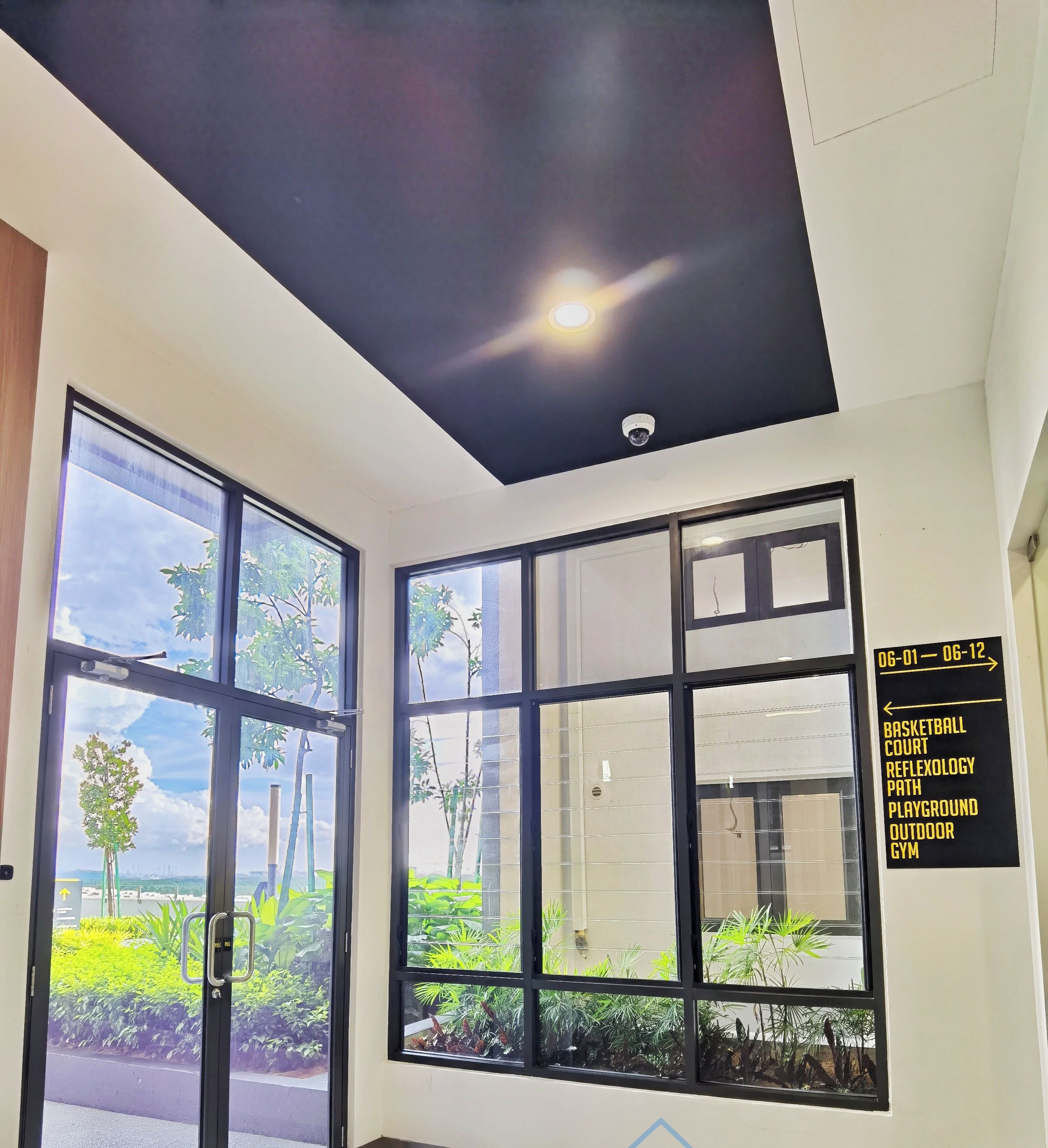 Un intérieur moderne avec de grandes fenêtres, un luminaire au plafond et un panneau indiquant les équipements disponibles, comme un terrain de basket et une salle de sport.