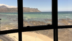 A coastal view through a window, including a beach, ocean, and distant mountains.