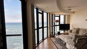 A spacious room with large windows offering a view of the ocean, a comfortable sofa, and a flat-screen TV.
