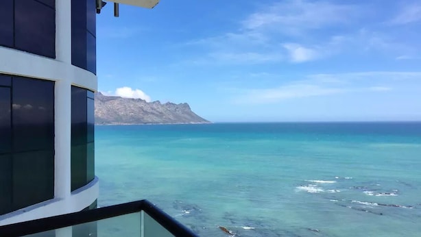 A modern building with large windows overlooking a clear blue sea and a distant mountain.