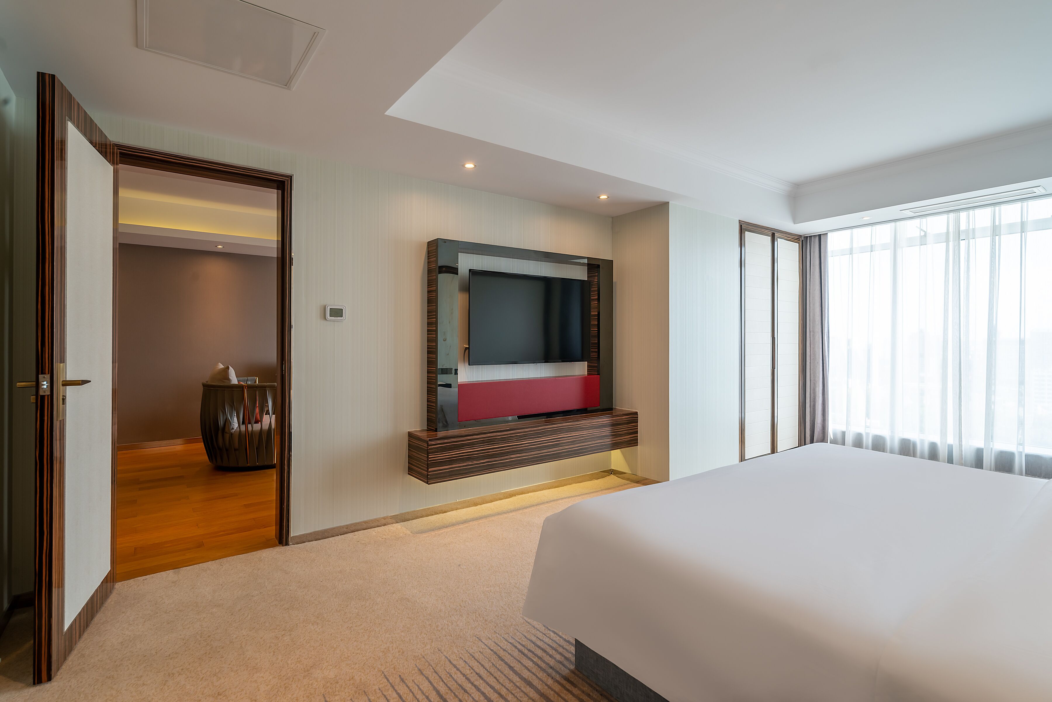 Ein Hotelzimmer mit einem großen Bett, einem an der Wand montierten Fernseher, Holzboden und Blick ins Freie durch das Fenster.