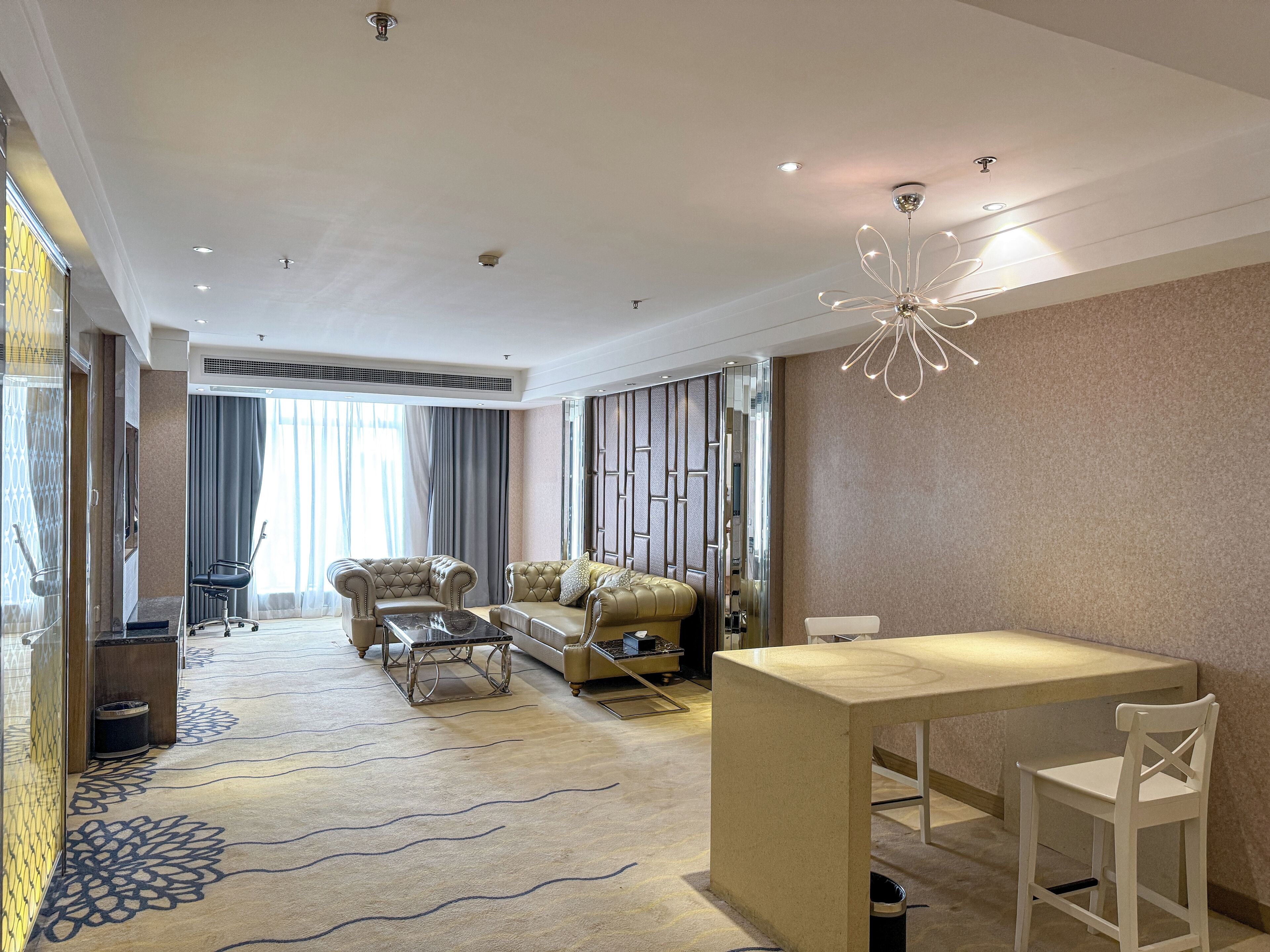 A modern hotel room with a large bed, a sofa, a coffee table, and a dining area.