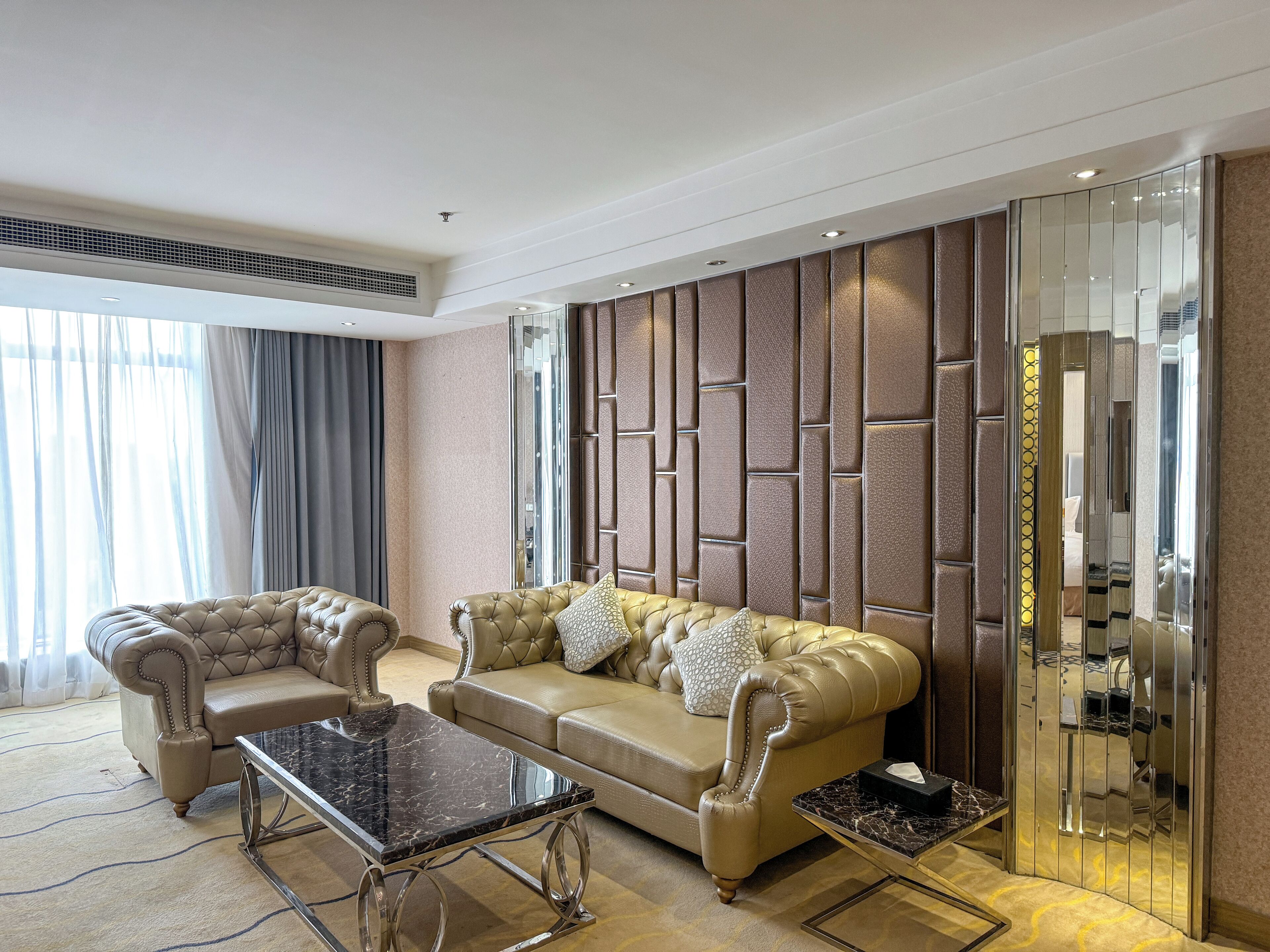 A spacious living room with a beige sofa, two armchairs, and a marble coffee table.