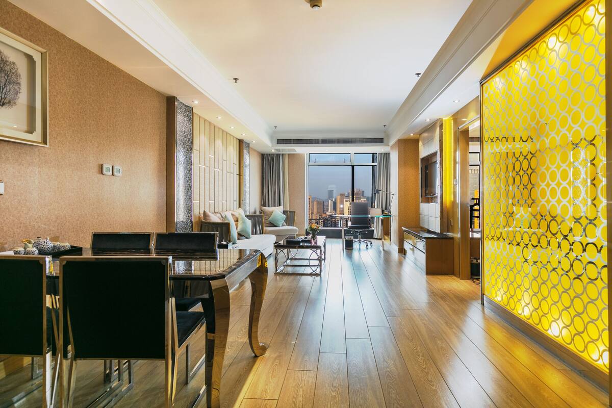 A spacious hotel lobby with a dining area, sofas, and a view of the cityscape through large windows.