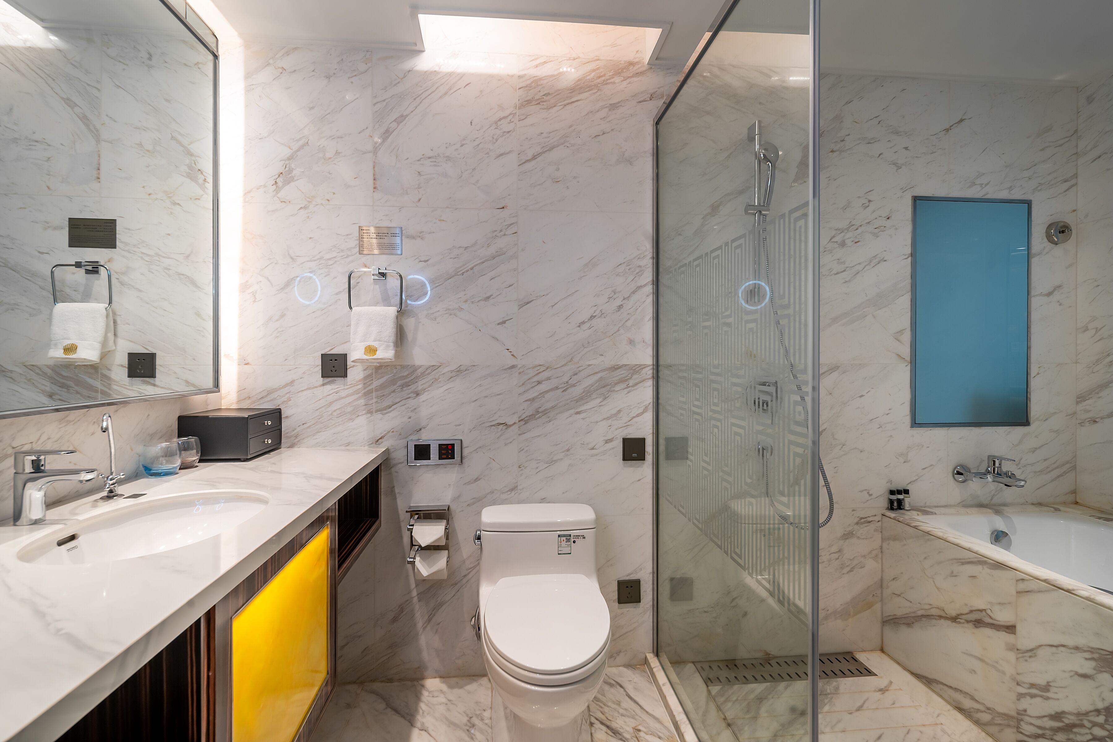 A modern bathroom with a marble floor, dual sinks, a toilet, a glass-enclosed shower, and a blue-tinted mirror.