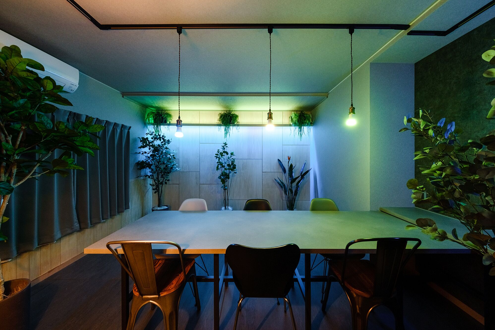 Une salle de conférence avec une longue table, quatre chaises, des plantes suspendues et des luminaires suspendus.