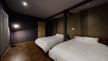 Habitación de hotel con dos camas, piso de madera, pared oscura con papel tapiz estampado y una lámpara en el techo.