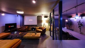Una sala de estar moderna con una pantalla grande mostrando 'NETFLIX', sofás de cuero, una mesa de centro de madera y un comedor con mesa y sillas.