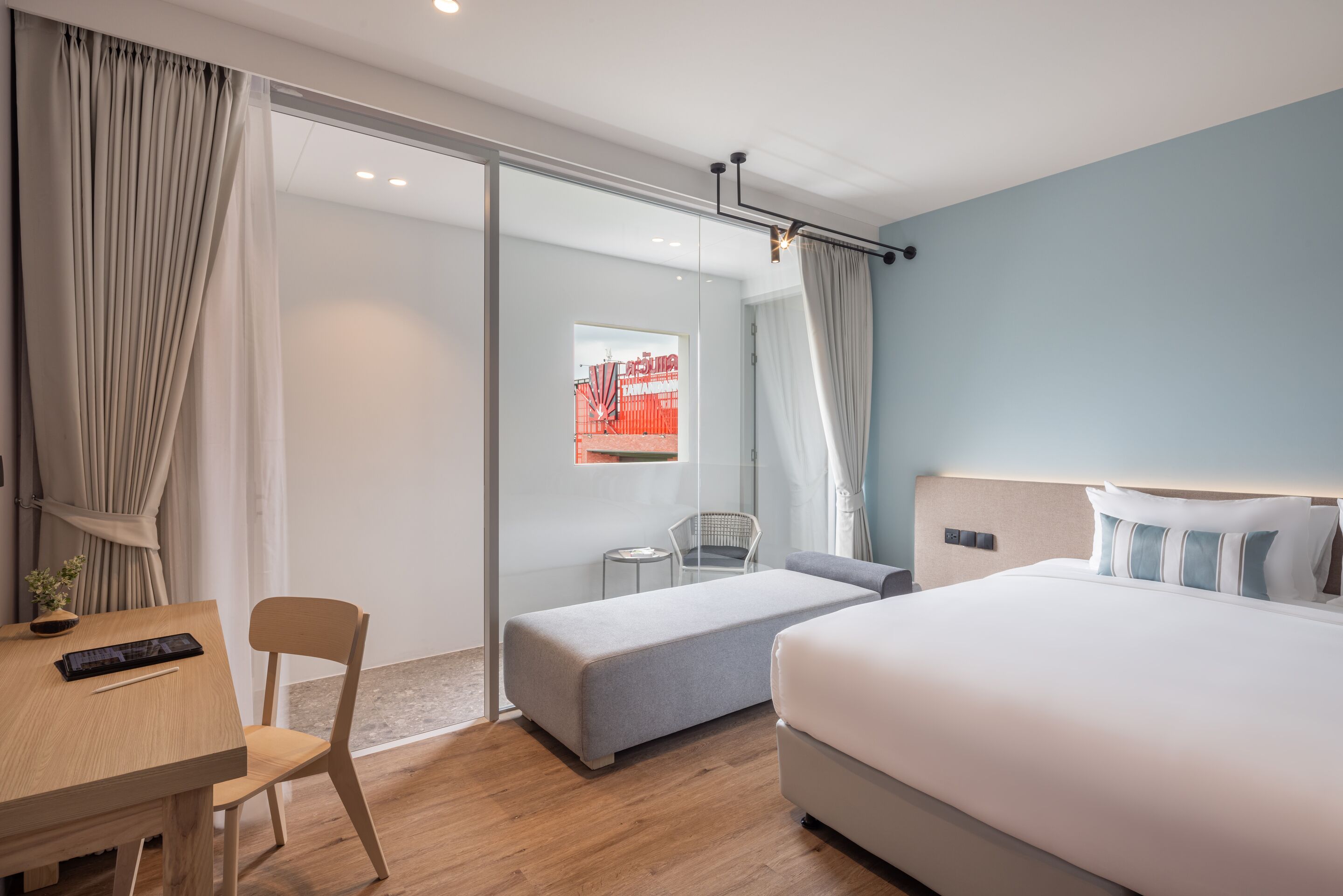 Habitación de hotel con cama, escritorio, silla, una mesita y vistas a un espacio exterior.