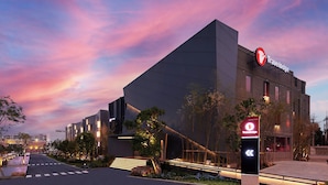 Un hôtel Travelodge moderne, avec une enseigne « Travelodge » bien visible, une entrée aménagée et un ciel dégagé.
