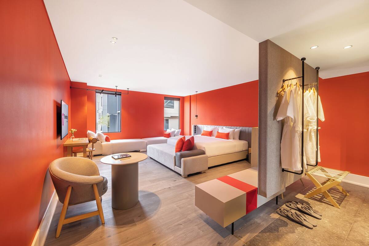 A modern hotel room with a sectional sofa, a bed, a round coffee table, and a seating area with a chair.