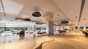 Un hall d’entrée spacieux, doté d’un sol poli, d’un éclairage moderne suspendu et d’un espace salon avec des meubles contemporains.