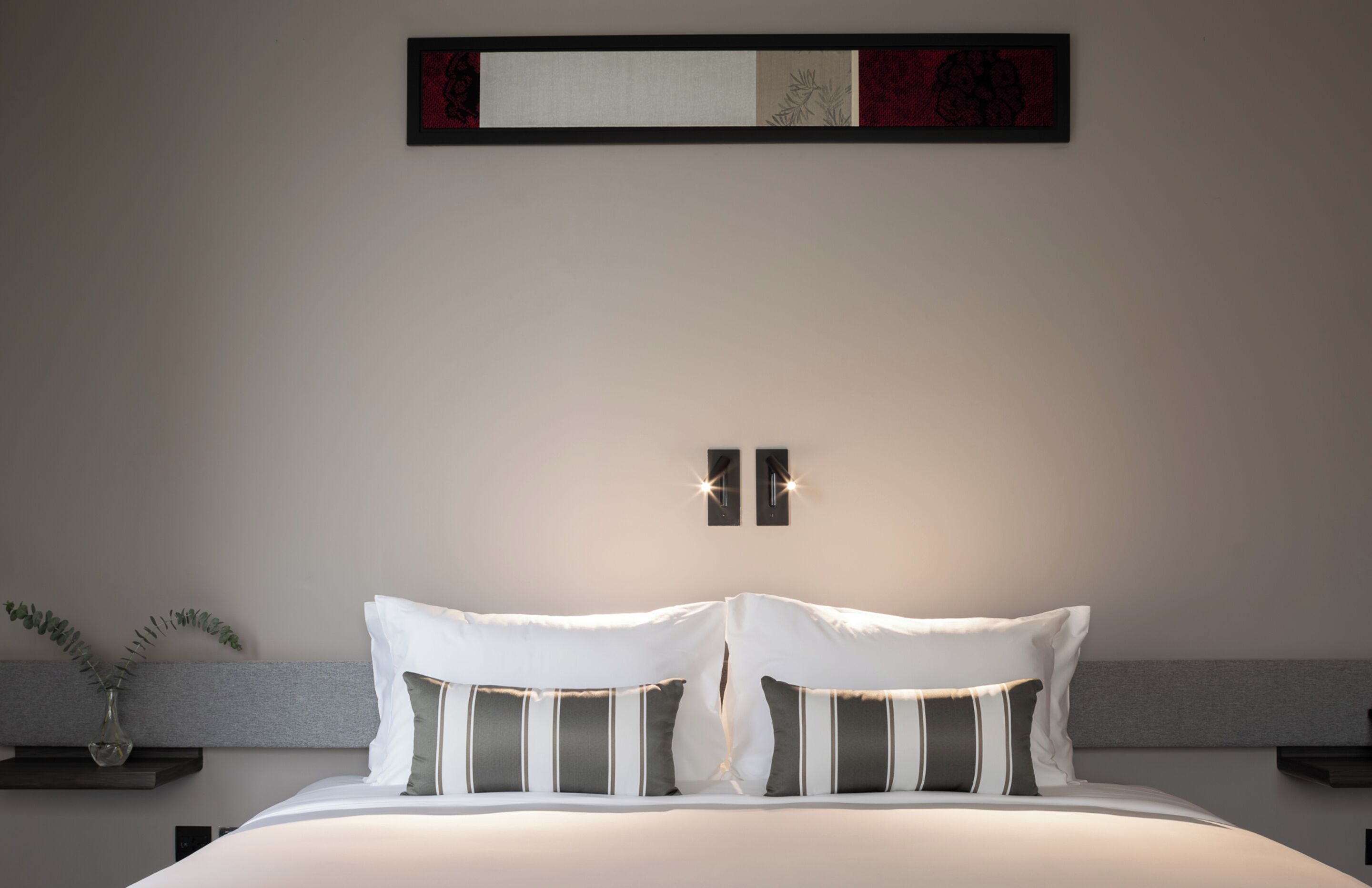 Un dormitorio moderno con una cama grande, dos mesitas de noche, una lámpara de pared y un adorno sobre la cama.