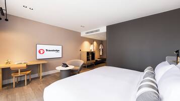 Habitación de hotel moderna con una cama grande, un escritorio, una silla y un televisor que muestra el logotipo de Travelodge.