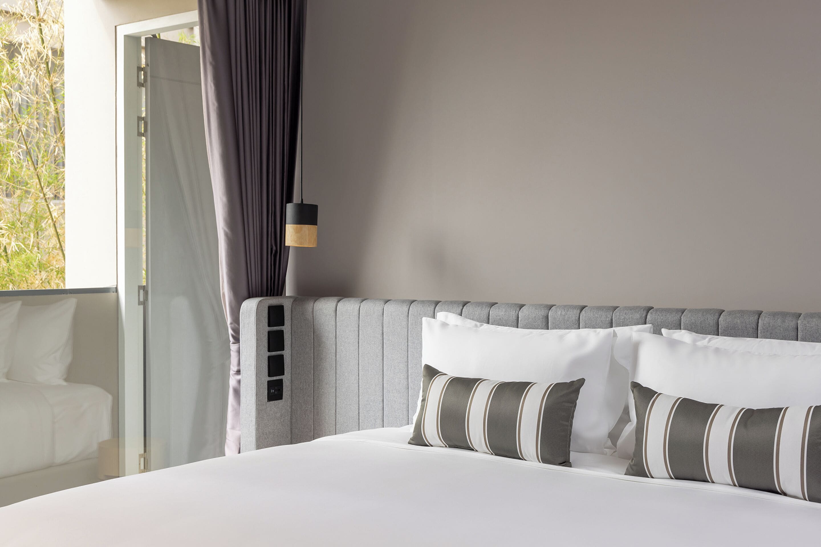 A neatly made bed with striped pillows, a grey headboard, and a bedside lamp.