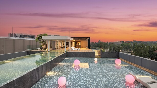 Une piscine à débordement située sur le toit, dotée d’un design moderne, un espace détente avec des sièges et une vue imprenable sur la ville au coucher du soleil.