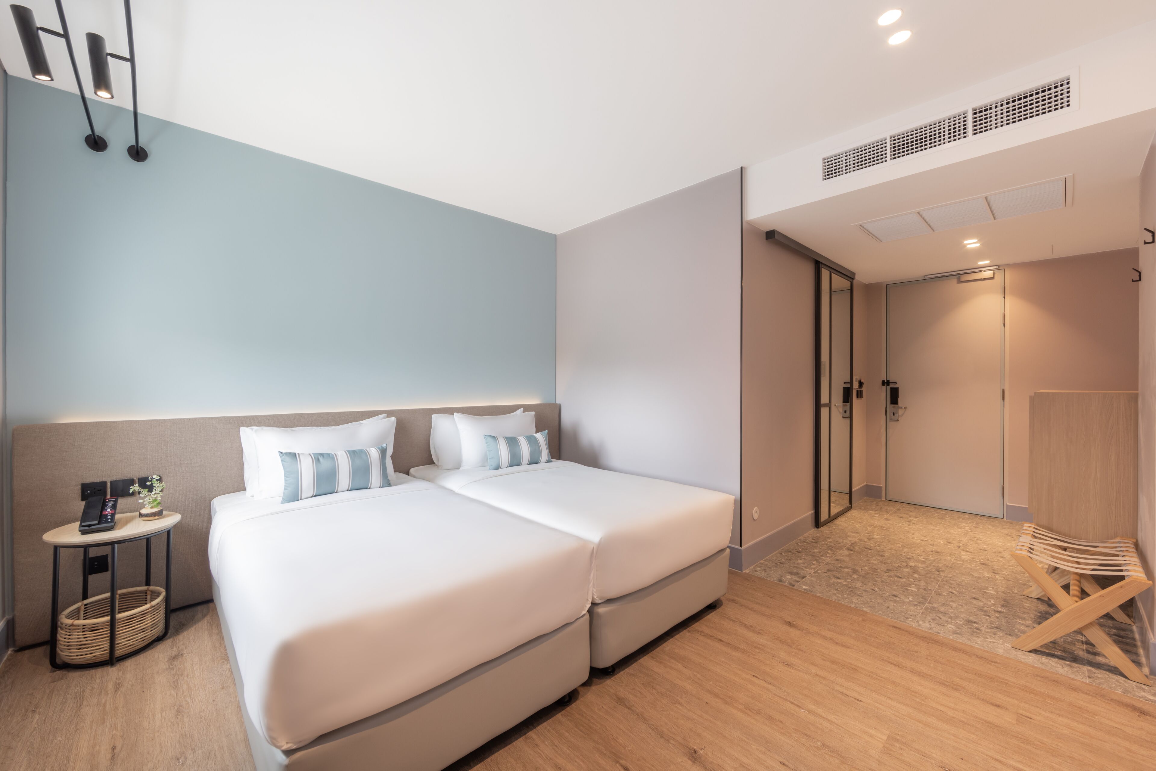 A modern hotel room with two beds, a small bedside table, a chair, and a door leading to a bathroom.