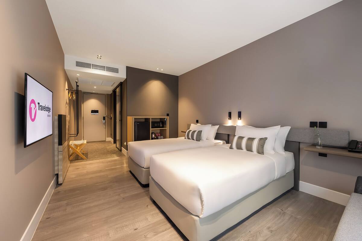 A modern hotel room with two beds, a TV, a desk, and a wardrobe.