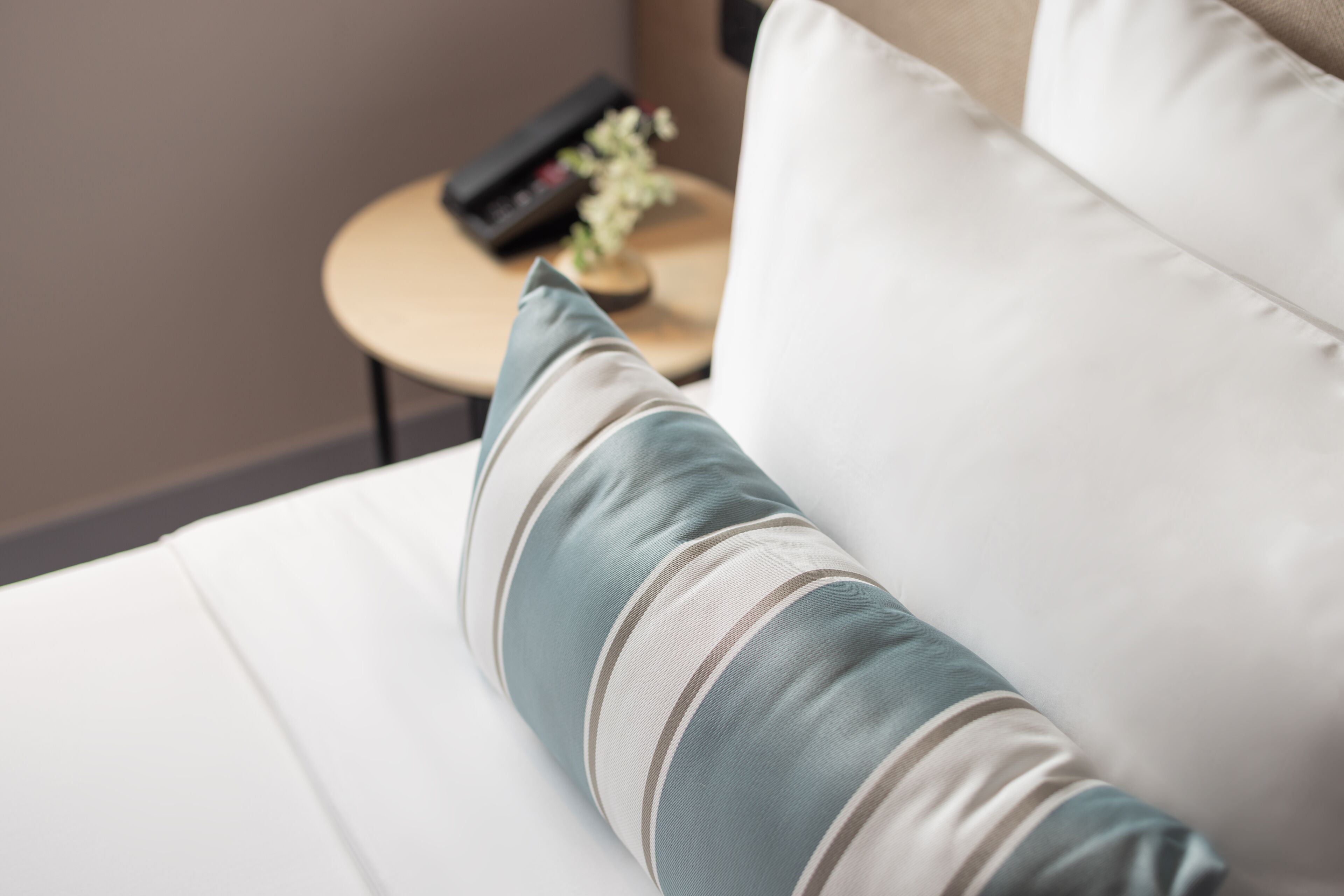 A close-up of a bed with a striped pillow and a remote control on a side table.
