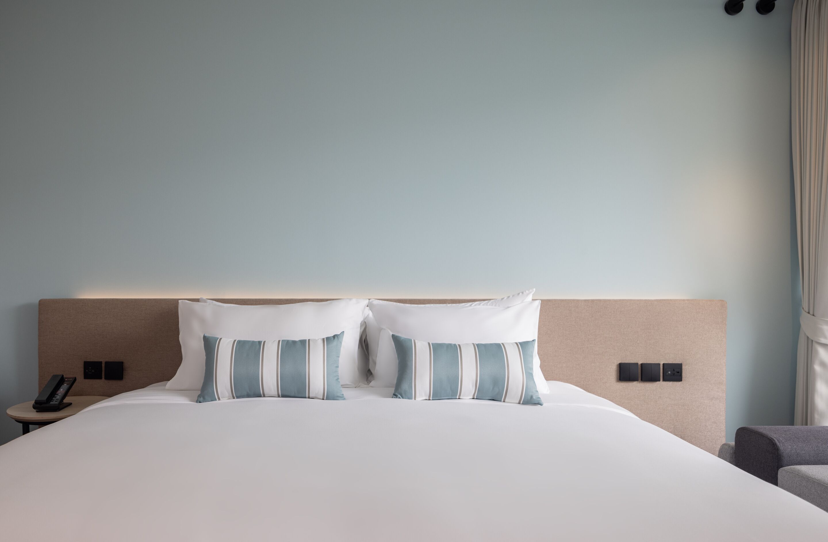 A hotel room with a large bed, two pillows, a bedside table with a phone, and a chair.