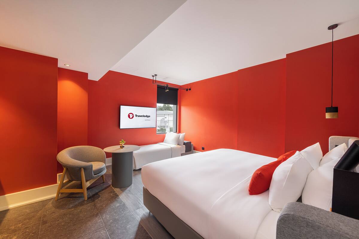 A modern hotel room with a large bed, a seating area with a chair and a small table, and a large window.