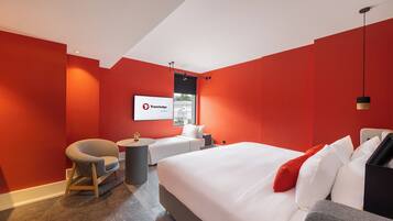 Una moderna camera d'hotel con un letto grande, una zona salotto con una poltrona e un tavolino, e un'ampia finestra.