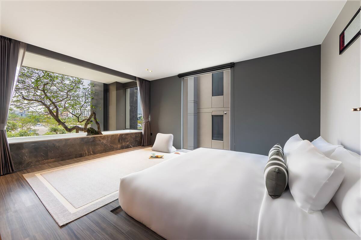 A modern bedroom with a large bed, a view of trees through the window, and a minimalist design.