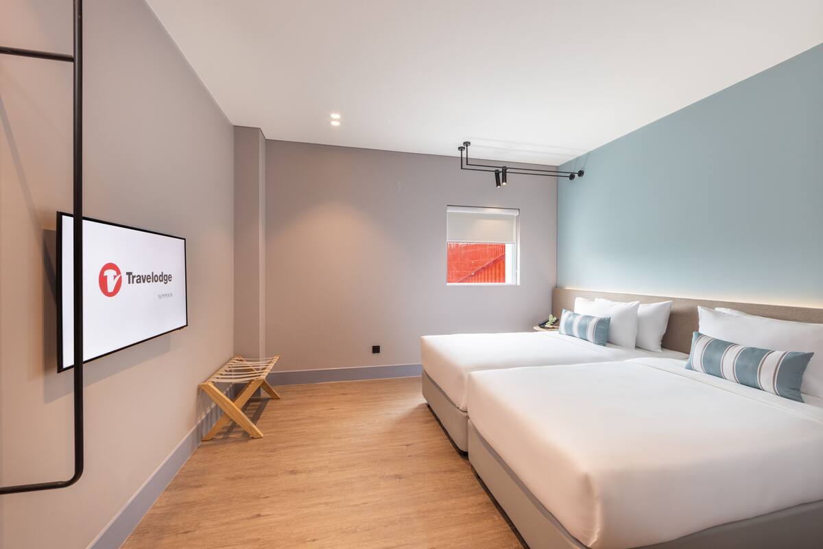 A modern hotel room with a large bed, a TV mounted on the wall, and a window with a view of a red building.