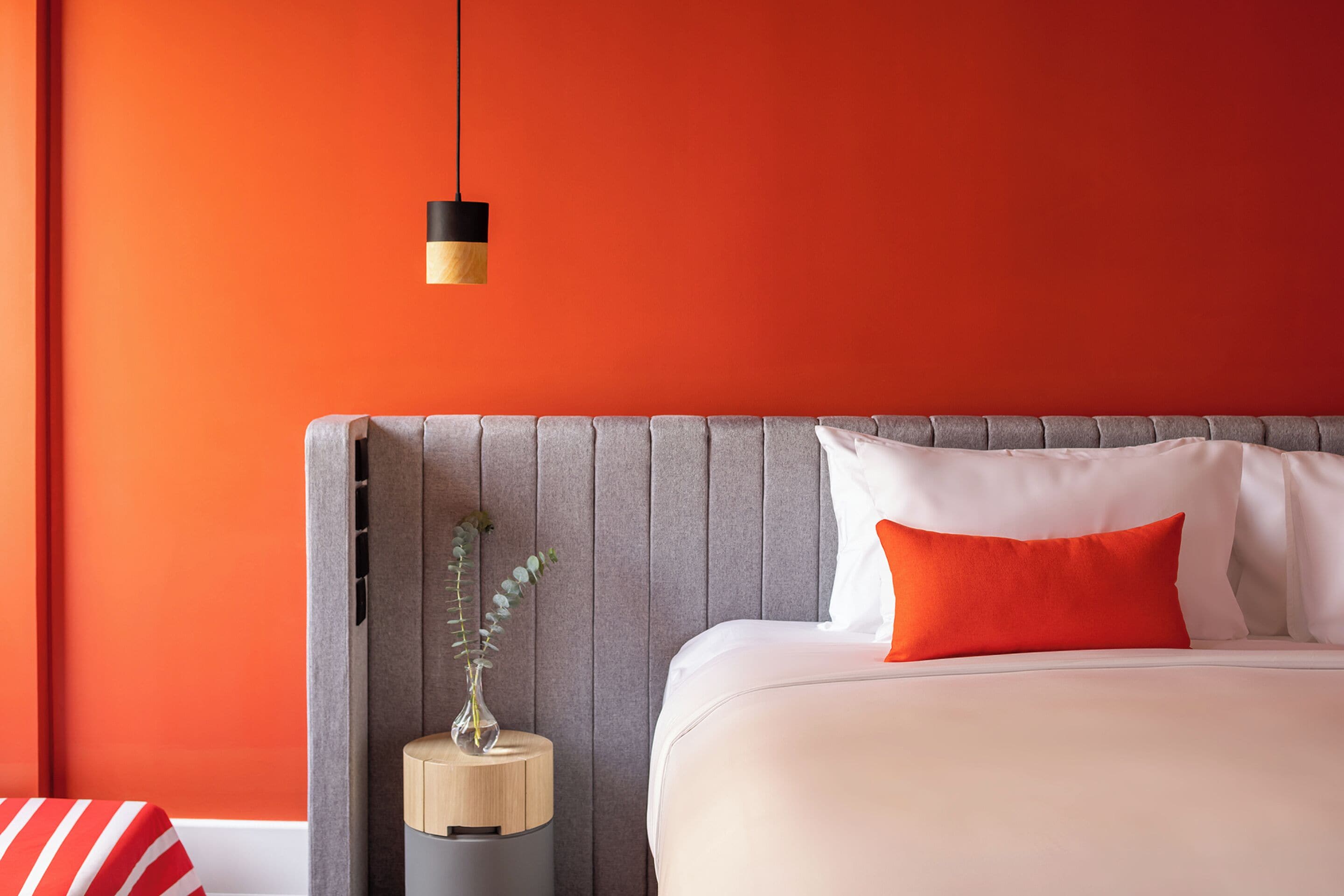 A modern bedroom with a large bed, a grey headboard, and a small bedside table with a vase.