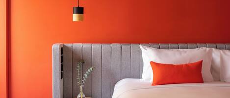 A modern bedroom with a large bed, a grey headboard, and a small bedside table with a vase.