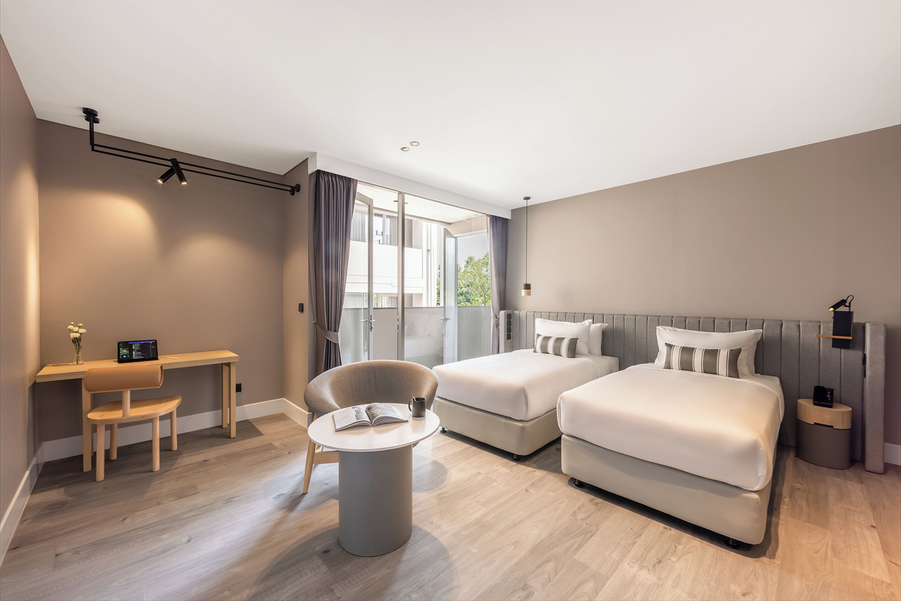 A modern hotel room with a desk, two beds, a chair, and a round table.