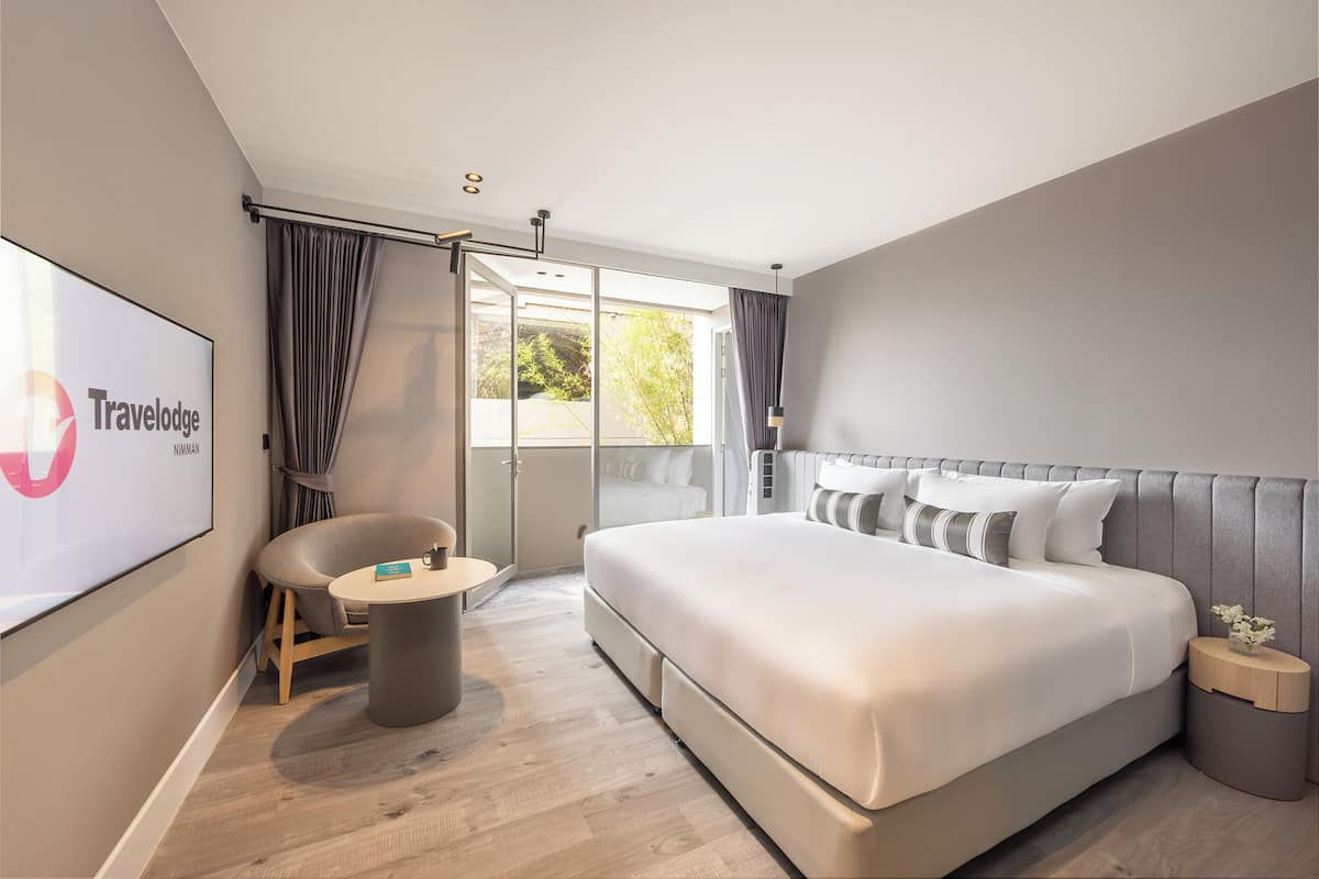 A modern hotel room with a large bed, a seating area, and a balcony with curtains.