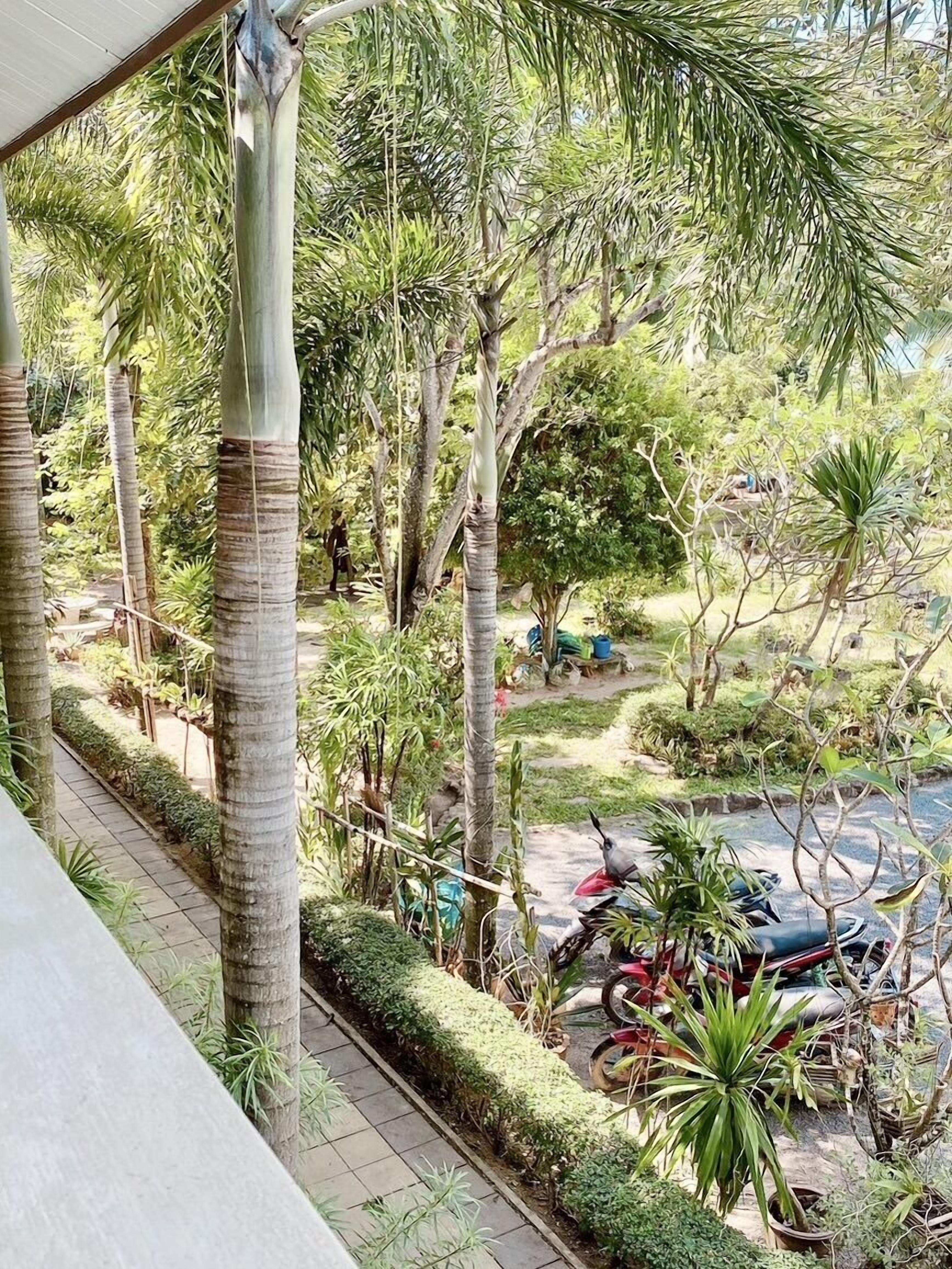 Un balcón con vista a un jardín, un sendero y motocicletas estacionadas.