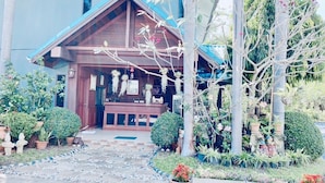 A house with a wooden porch, potted plants, and a stone pathway leading to the entrance. - Baan Karnjana Hotel Samui (Koh Samui)