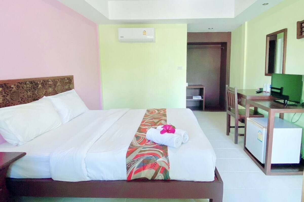 A hotel room with a bed, a desk, a chair, a television, and an air conditioning unit.