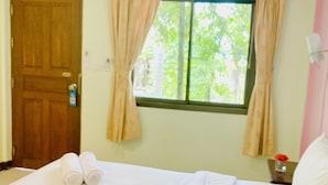 A hotel room with a bed, a window with curtains, a wooden door, and a small table with a vase of flowers. - Baan Karnjana Hotel Samui (Koh Samui)