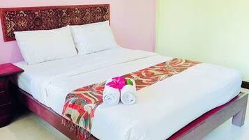 A neatly made bed with a patterned blanket and rolled towels, a wooden headboard, and an air conditioning unit on the wall.
