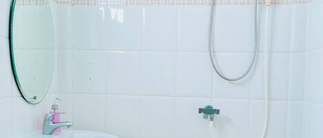 A bathroom with a white sink, a mirror, a shower with a control panel, and a tiled floor.