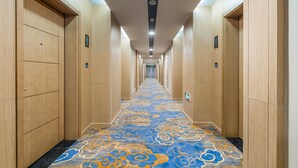 A hotel hallway with wooden paneling, a patterned carpet, and a long corridor leading to an elevator. - JOY FALL HOTEL (Qingdao)