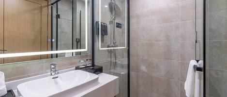 A modern bathroom with a large mirror, a white sink, a glass shower enclosure, and a towel rack.