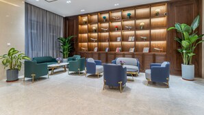 A modern lobby with a wooden bookshelf, comfortable seating, and potted plants. - JOY FALL HOTEL (Qingdao)
