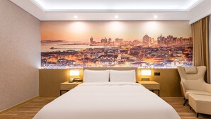A hotel room with a large bed, two bedside tables with lamps, a chair, and a cityscape mural on the wall. - JOY FALL HOTEL (Qingdao)