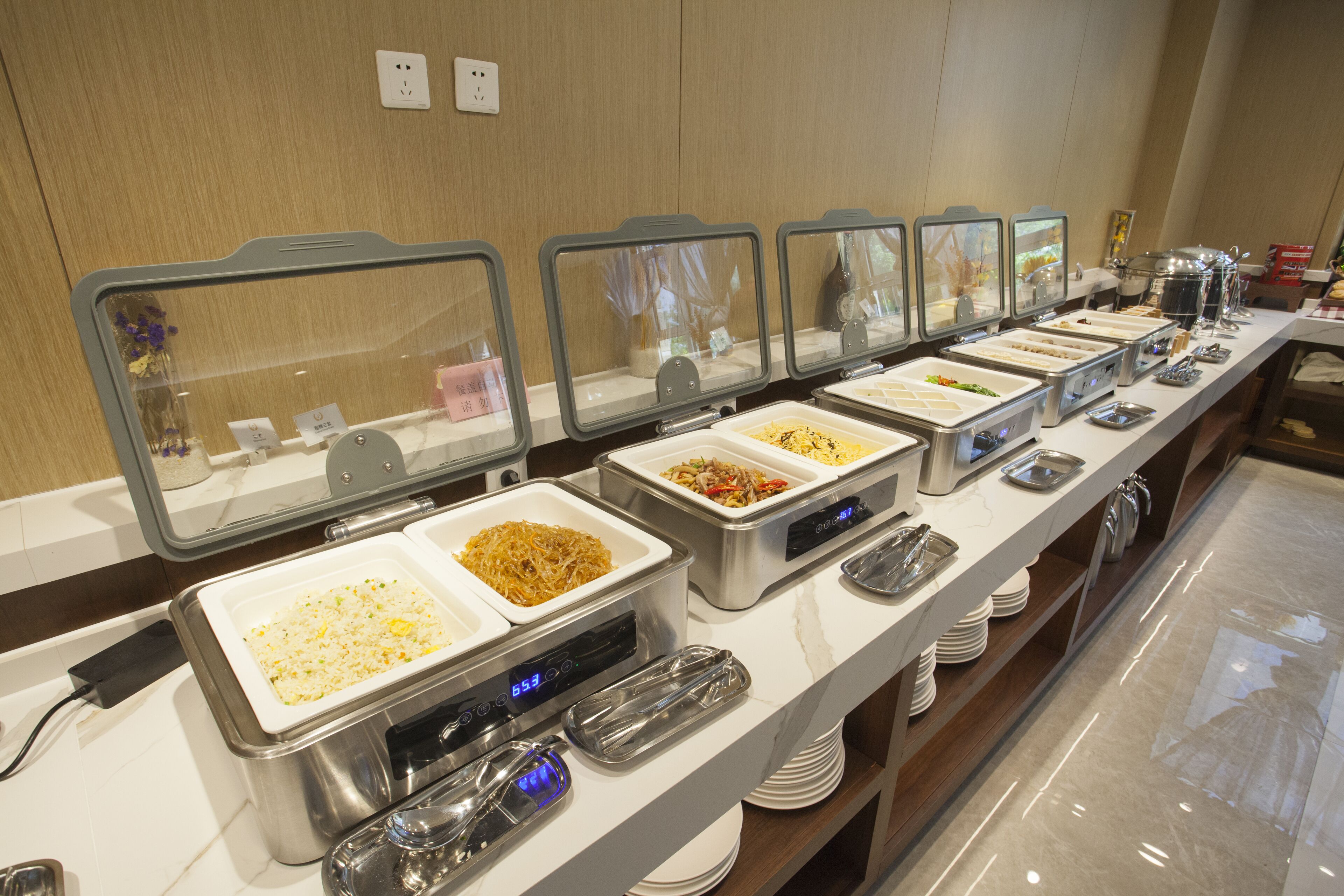 Un bufé con varias estaciones de comida, cada una con una cubierta de vidrio transparente y una pantalla digital.