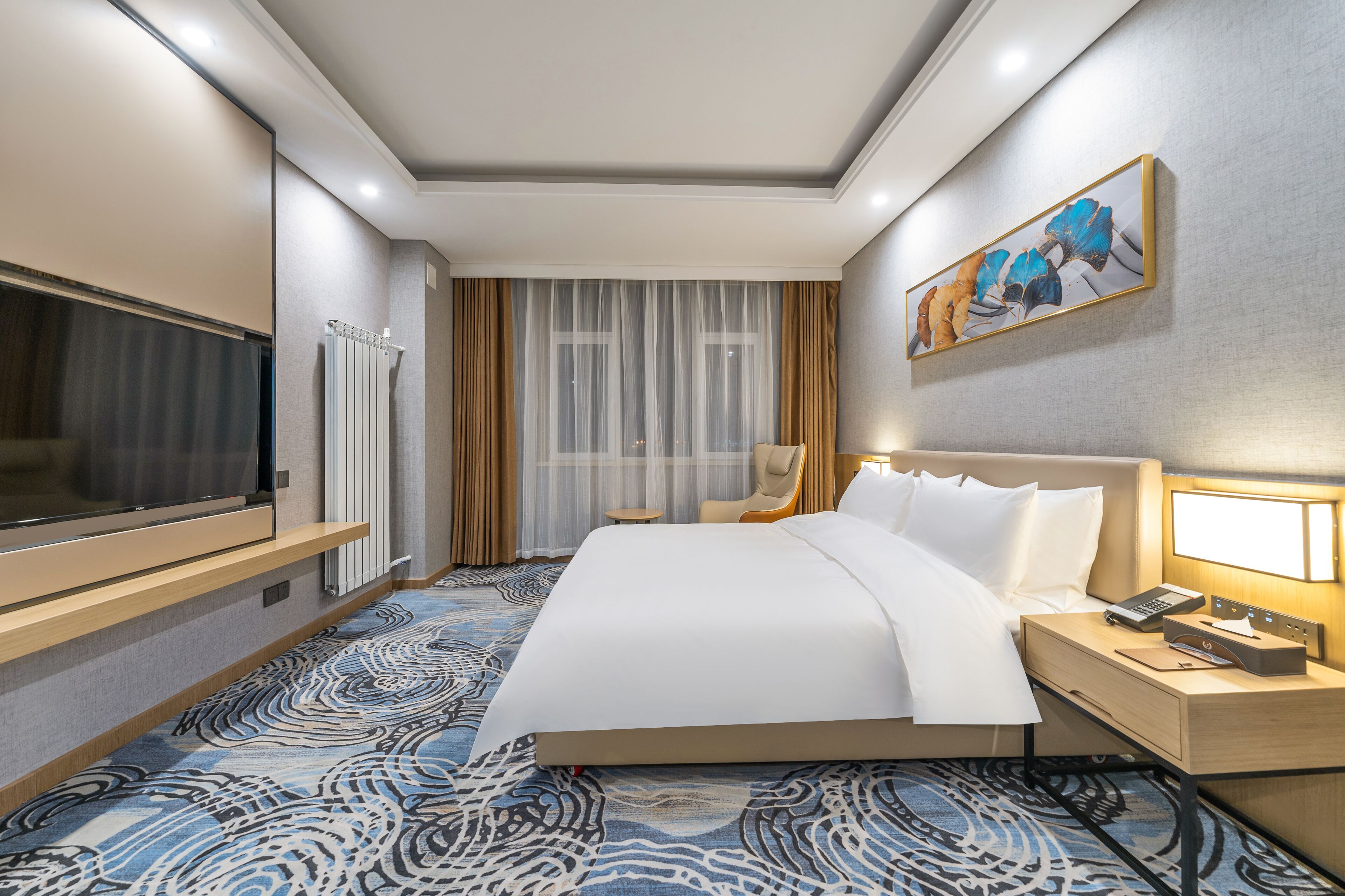 A hotel room with a large bed, a flat-screen TV, a bedside table with a lamp, and a painting on the wall.