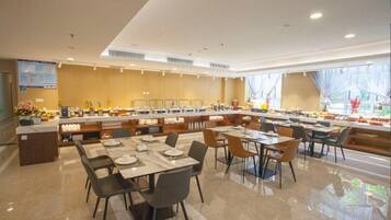Un comedor moderno con varias mesas y sillas, una barra de buffet y un amplio ventanal que proporciona luz natural.