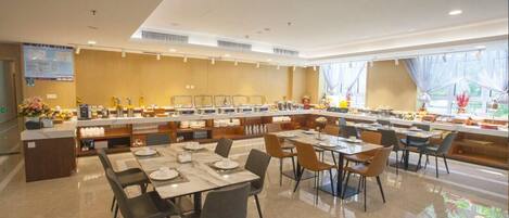 Un comedor moderno con varias mesas y sillas, una barra de buffet y un amplio ventanal que proporciona luz natural.