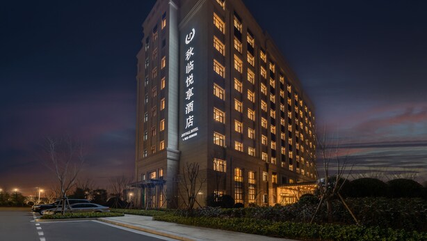 A tall hotel building with illuminated windows and a sign in a foreign language. - JOY FALL HOTEL (Qingdao)