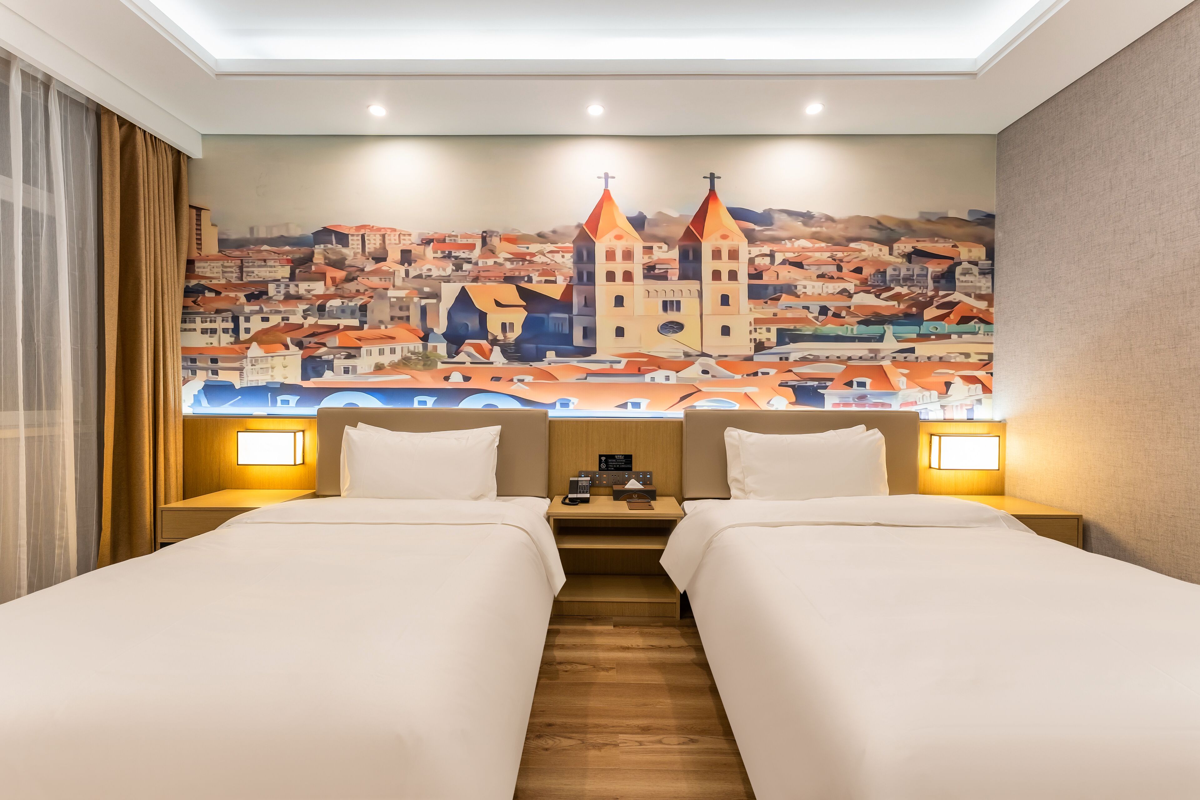 A hotel room with two beds, a mural of a cityscape, and bedside lamps.