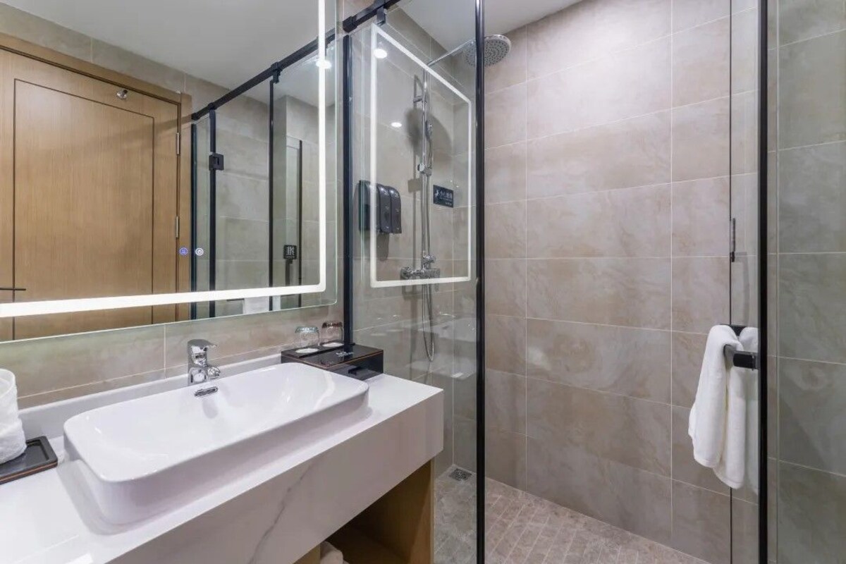 Une salle de bain moderne avec un grand miroir, un lavabo blanc, une douche en verre et un porte-serviettes.